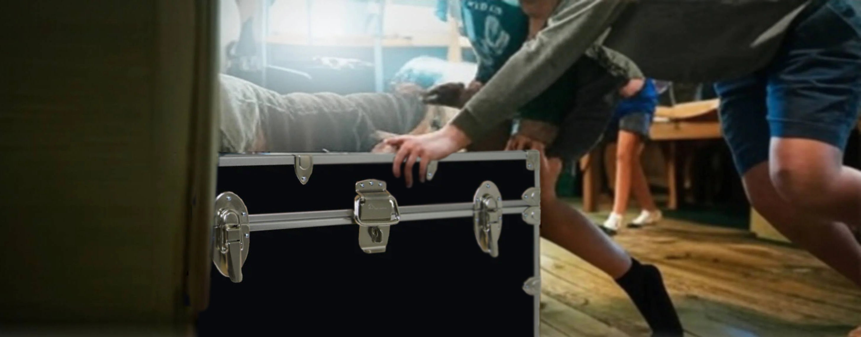 Person reaching into a black suitcase in a room with other people and furniture.