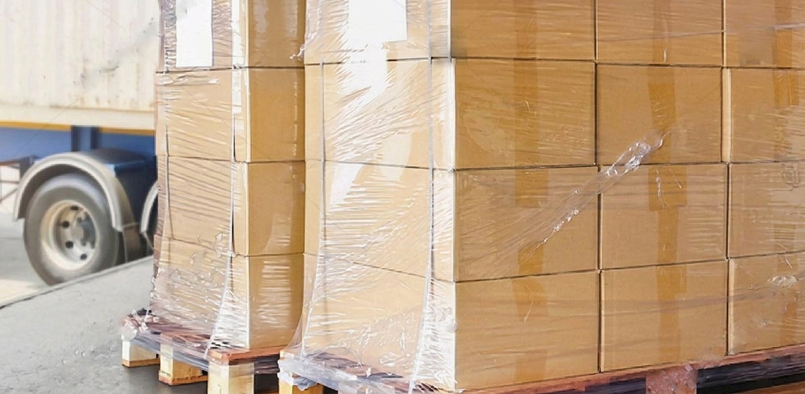 Stacks of cardboard boxes on a pallet with a truck in the background