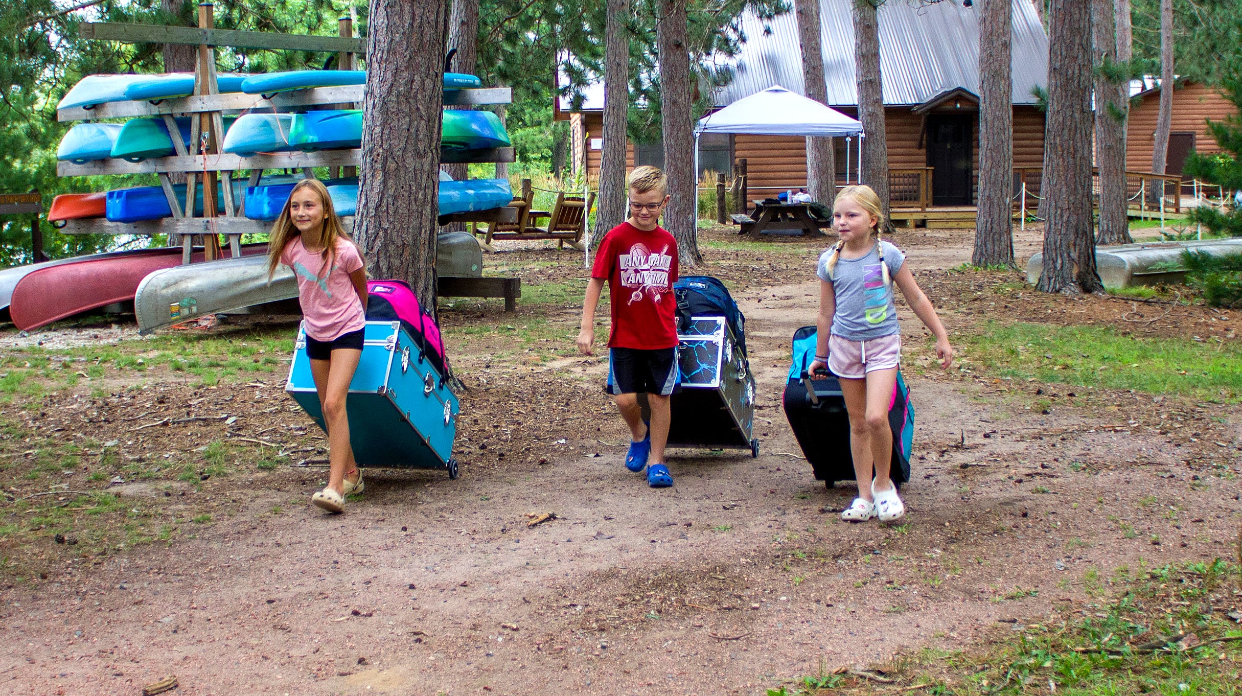 Campers roll their camp trunks behind them at a summer camp scene